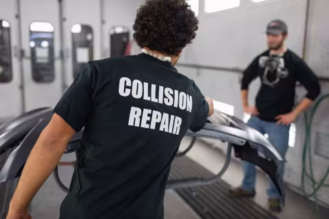 Collision repair student in a branded shirt working on a car bumper in the auto shop