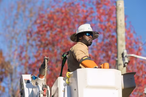 Central Piedmont student working as an electrical lineworker in bucket truck with fall foliage in background.