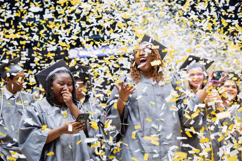 Graduates celebrating as gold and black confetti falls
