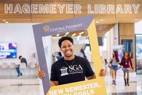 SGA President Akai Martin holding a sign that says "New Semester, New Goals"