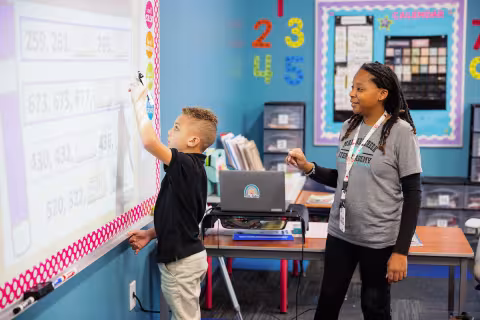 Teacher in training standing at the whiteboard with a young student