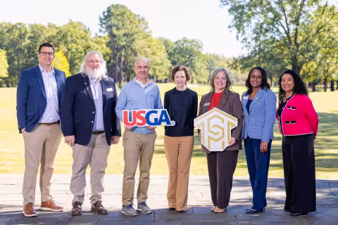 Members of Central Piedmont and USGA staff holding logos on golf course